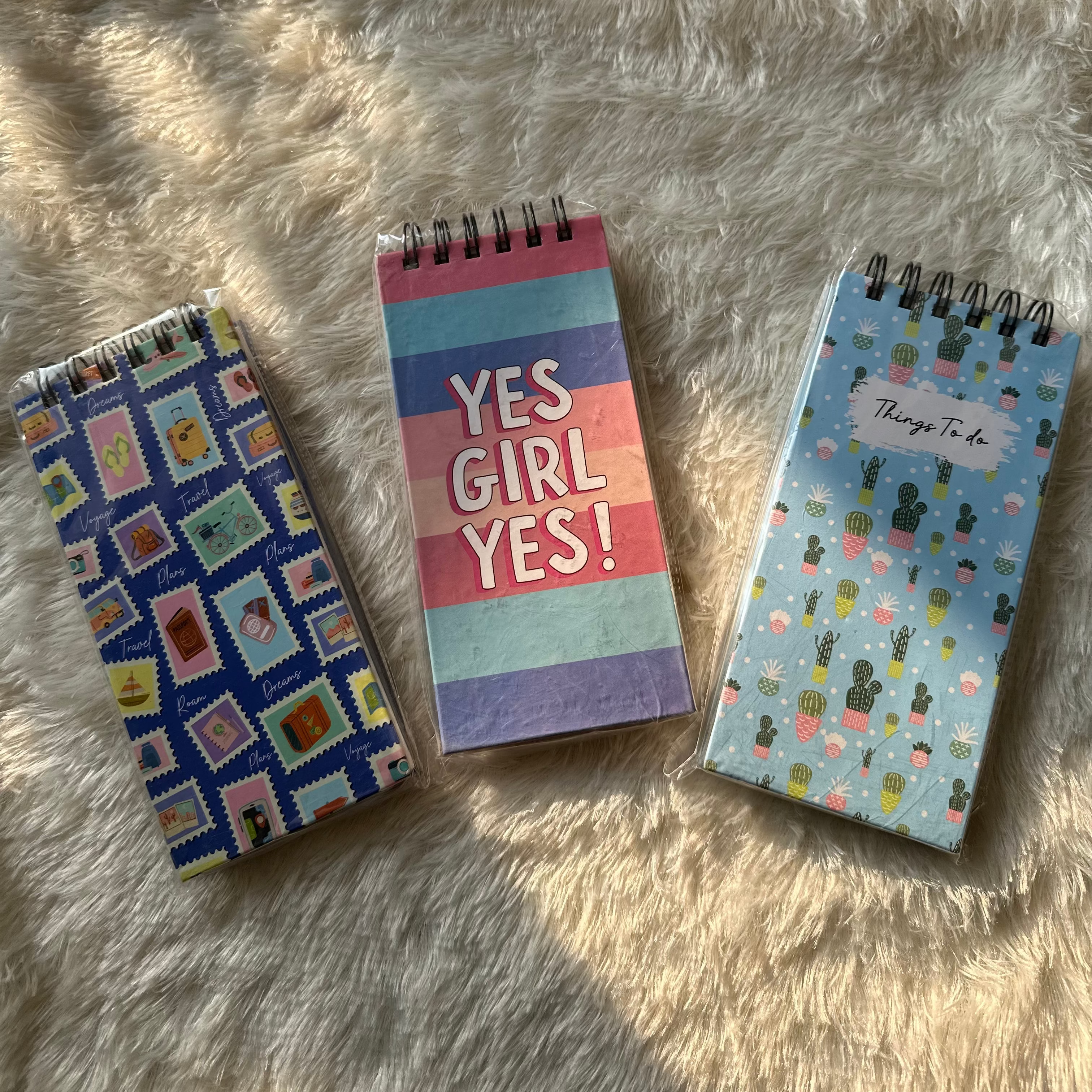 Three small notebooks with different designs on a fluffy white surface